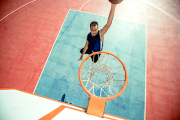 Young man jumping and making a fantastic slam dunk playing streetball, basketball. Urban authentic.