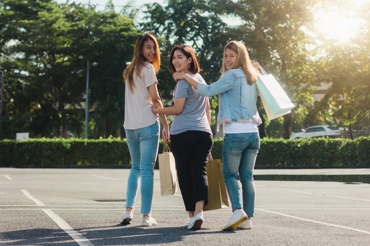 Group of young Asian Woman shopping in an outdoor market with shopping bags in their hands. Young women show what they got in shopping bag under warm sunlight. Group outdoor shopping concept.