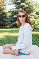 Obraz premium Portrait of beautiful pensive young European Caucasian woman with red hair wearing sunglasses. Young girl teenager outside looking in camera