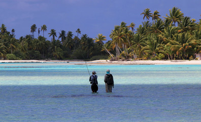 Fly-fisherman and guide walking on flats in turquoise waters in French Polynesia