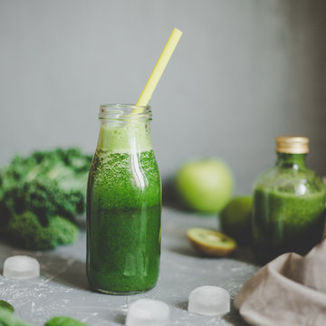 Healthy green smoothie with ingredients and ice cubes on gray background