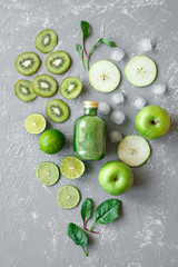 Healthy green smoothie with fresh green fruits and spinach leaves on gray background, top view