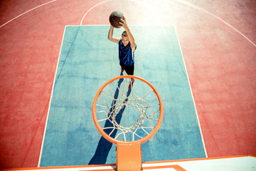 Young man jumping and making a fantastic slam dunk playing streetball, basketball. Urban authentic.