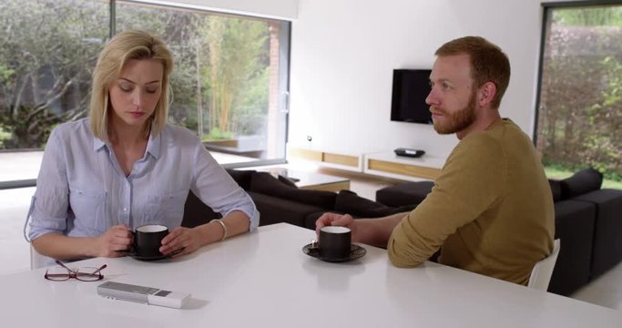 Attractive couple having awkward coffee, not speaking to each other in contemporary house, in slow motion