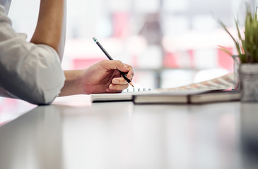 Close up short of businessman hand holding pencil while sitting at white desk at workplace
