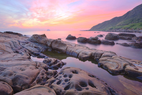 Beautiful sunrise sky reflected on the peaceful seawater at a rocky beach in northern Taiwan~Scenery of the unique coast with bizarre rock formations under dramatic dawning sky (Long Exposure Effect)
