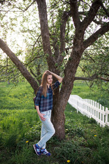 A young beautiful girl with long hair in a blue shirt in a cage and blue ragged jeans near the blossoming apple tree. Spring