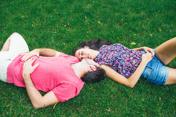 Smiling couple happy relaxing on green grass. Young couple lying on grass outdoor have fun in the sunny summer day.