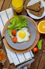 English Breakfast: fried egg, juice, cherry tomatoes, lettuce, grain bread, sauce, top view.
