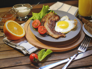 English Breakfast: fried egg with bacon, orange juice, tomatoes, zernovoi bread, lettuce leaf, top view.