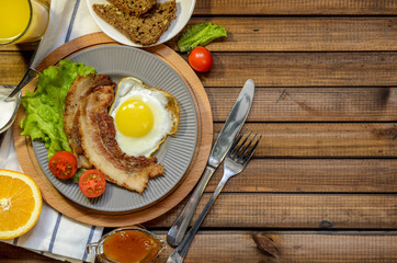 The concept of the English Breakfast: fried egg with bacon, orange juice and vegetables. Free space for text, top view.