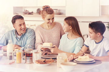 Thank you mom. Charming woman keeping smile on her face and looking at her daughter while giving plate with cake