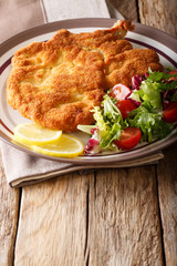 Fried veal cutlet Milanese with lemon and fresh salad of tomatoes and lettuce close-up on a table. vertical