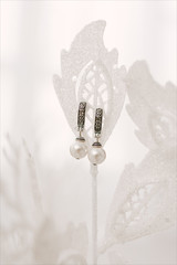 Women's wedding earrings hang on leaf and light background, selective focus