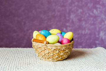 Dyed eggs lie in a wicker basket on a table