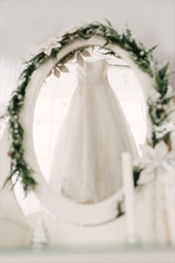 the wedding dress hangs on a hanger and is reflected in the mirror, the bride's morning