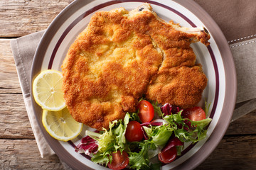Veal milanese (cotoletta alla milanese) with lemon and fresh vegetable salad close-up. horizontal top view