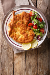veal Milanese with lemon and fresh salad of tomatoes and lettuce close-up. Vertical top view