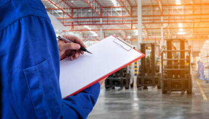 Worker checking document in front of the forklift at warehouse import export business.