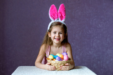 A girl in a rim with rabbit ears plays with dyed eggs and laughs