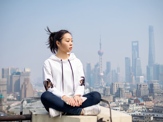 Beautiful young brunette woman sit on top of mansion roof with blur Shanghai Bund landmark buildings background. Emotions, people, beauty and lifestyle concept.