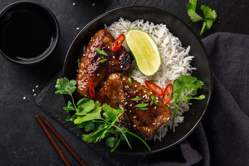 bowl of teriyaki chicken wings and rice served with lime, cilantro and sesame seeds