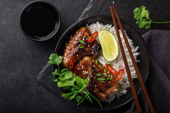bowl of teriyaki chicken wings and rice served with lime, cilantro and sesame seeds