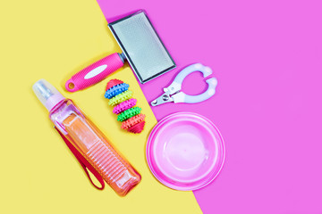 Pet accessories concept:  bowl, toys, brush, bottle of water and nail scissors on yellow background.