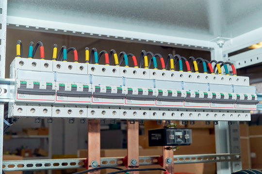 A range of electrical wires or cables are connected to the modular circuit breakers. Black wires are marked in different colors. In the background, the design of the electrical Cabinet with busbars.