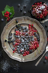 Fresh red and black currant, black raspberries garnish sugar powder, branch red currant in platter on black. Top view.