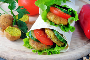 Falafel and vegetables wrapped in lavash on a light cutting board. Close-up view.