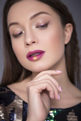 Caucasian brunette woman with creative make up (sequins and glitter on her face), prepared for stage show. She wearing shiny clothes. Neutral background