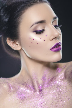 Close up beauty portrait of a fantasy art theme: Star Wars cosplay. Princess Leia hairstyle with purple glitters and stars all over woman face and body. Creative violet backlight, studio image