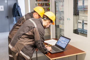 Two maintenance engineers inspect relay protection system with laptop comp