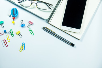 Top view of laptop, blank notebook, paper clips  and smart phone with white background and copy space.