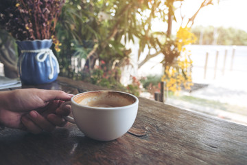 Closeup image of a hand holding a coffee cup on vintage wooden table in cafe