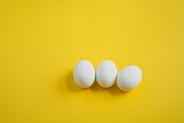 three white wooden eggs on yellow background, Easter holidays decoration
