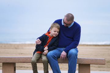boy with father talking on a bench by the sea in spring