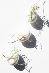 White minimalistic Easter eggs decorated with twine and flowers of gypsophila on a white background in bright light with deep shadows. Easter concept. Top view, flat lay