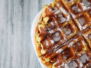 Belgian waffles in a white plate on a light wooden table. Homemade dessert