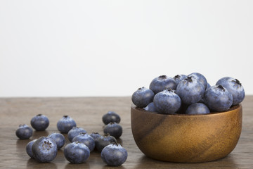 Blueberries in wooden bowl on wooden table white background copyspace.
