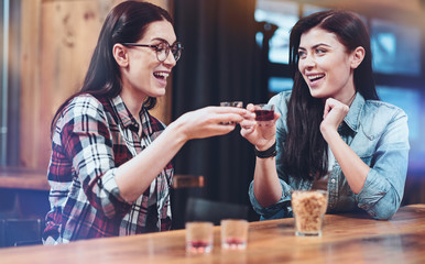 Friday night. Positive happy joyful woman sitting opposite each other and drinking shots while resting on Friday night