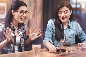 Having fun. Delighted positive young woman smiling and drinking alcohol while having fun with her friend