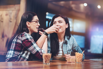 Friends forever. Positive joyful female friends sitting at the bar counter and drinking together while relaxing on Friday night