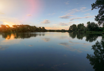 Beautiful sunset, sky with clouds above lake with trees around.