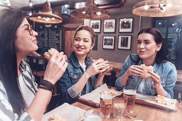 Junk food. Happy cheerful positive women sitting together and feeling happy while enjoying their burgers