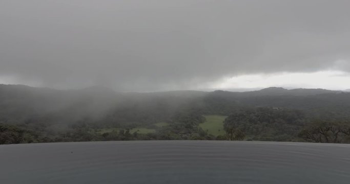 An aerial view of an infinity pool with a view of lush green and misty mountains and fields.