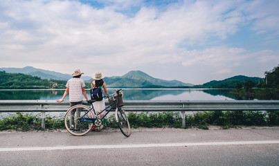 couple traveler standing beside bicycle and happy for view of nature near the lake  on vacation background is mountain.
