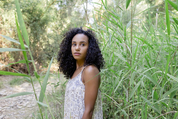 portrait outdoors of a beautiful young afro american woman at sunset. Green background. Lifestyle