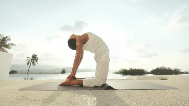 Woman training yoga asana Ustrasana on outdoor terrace with panoramic sea view